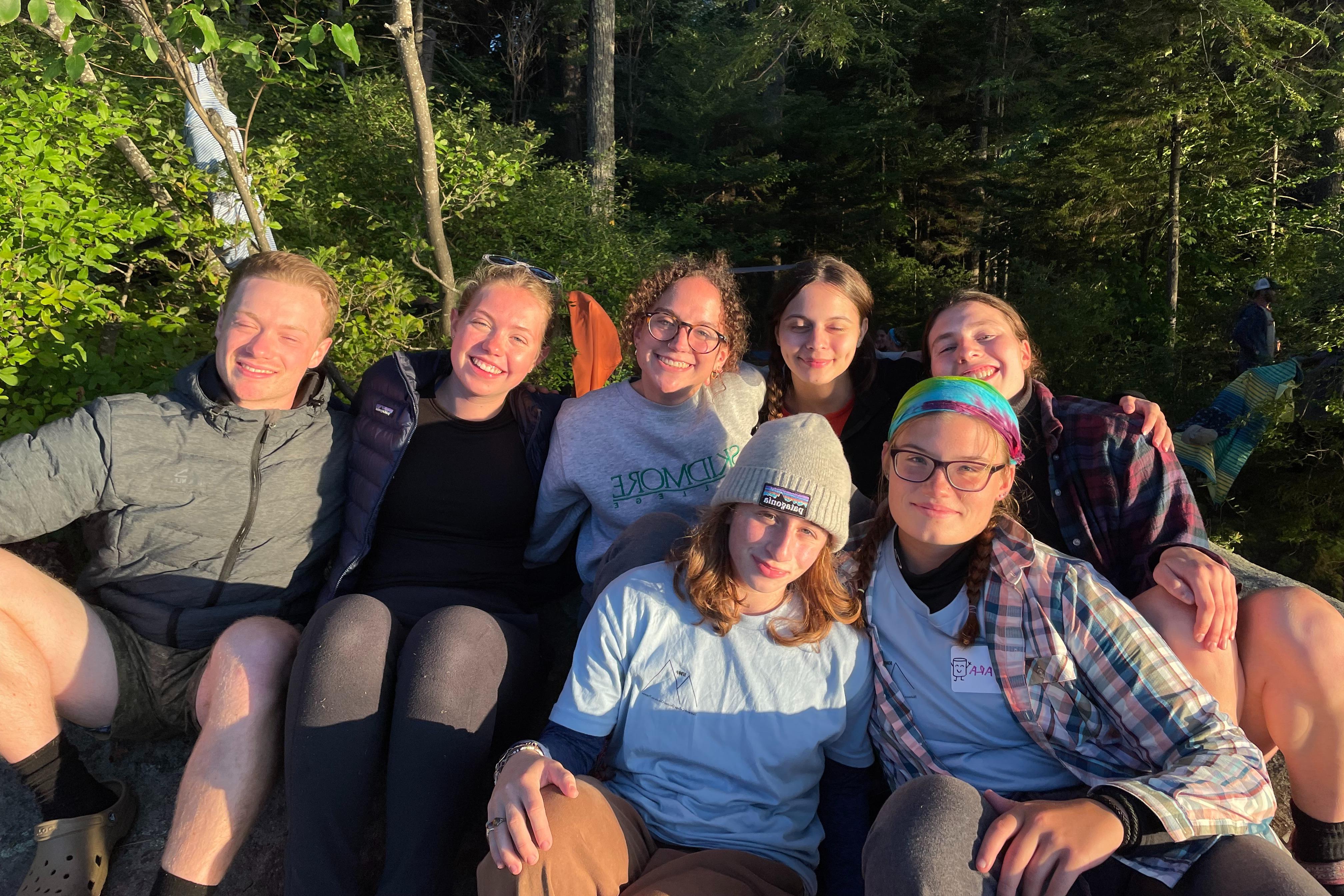 七名学生(包括凯蒂·汉密尔顿)坐在那里，对着阳光微笑. 在背景中可以看到茂密的树木和绿色植物.